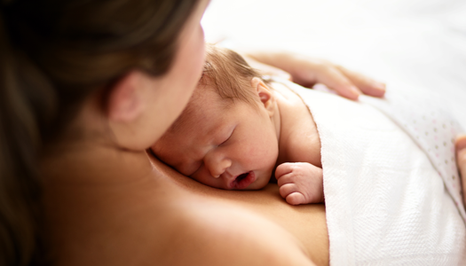 A woman holds her newborn, practicing the baby-friendly technique of skin-to-skin contact.