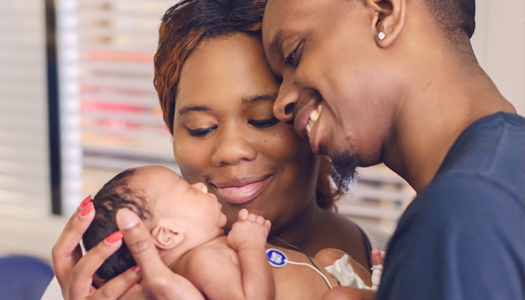 A wife and husband gaze lovingly at their newborn