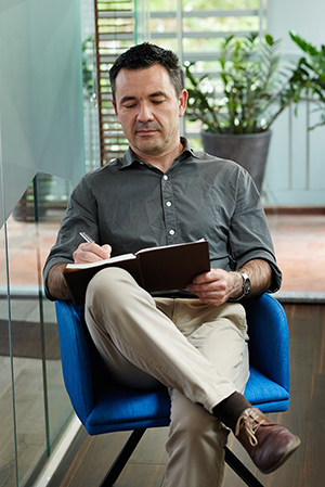 Man sitting in chair while writing in notebook. 