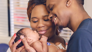 A mother and father hold and gaze lovingly at their newborn.